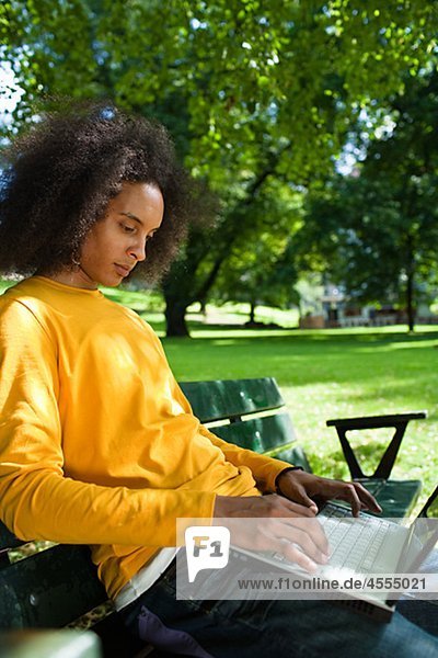 Young man with afro hair sitting on bench and using laptop