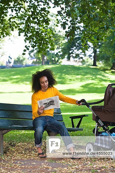 Junger Mann mit Kinderwagen auf Bank sitzen und lesen Zeitung