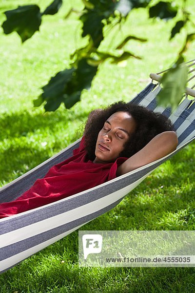 Young man with afro hair sleeping in hammock in park