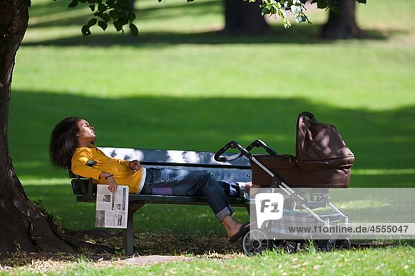 Young man with baby carriage relaxing on bench in park