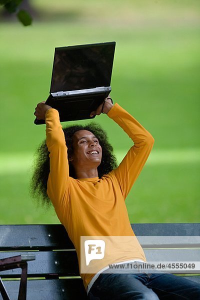 Young man with afro hair sitting on bench and lifting laptop