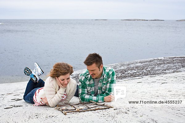 Mid adult couple playing tic-tac-toe on beach