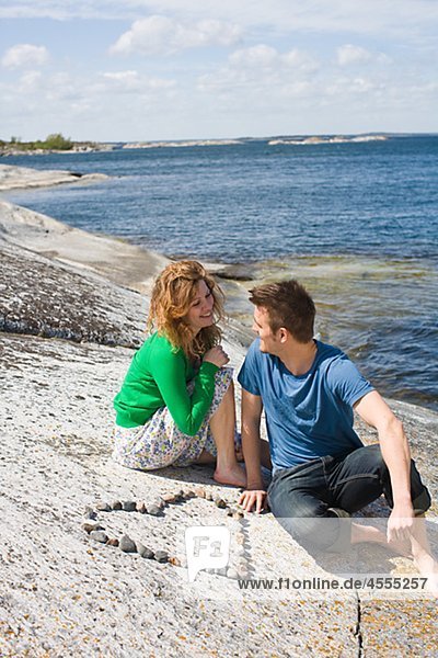 Mid adult couple sitting on beach near heart made from pebbles