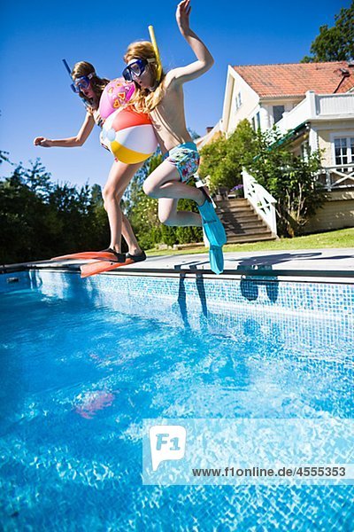 Sisters in scuba mask jumping into swimming pool