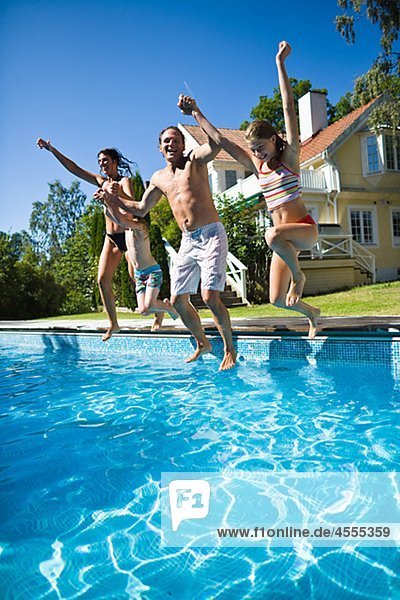 Family jumping into swimming pool while holding hands
