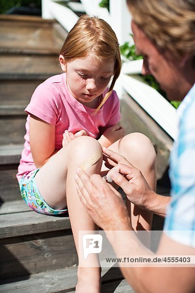 Father sticking adhesive bandage on his daughters knee