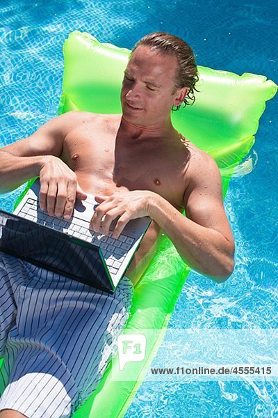 Man floating on inflatable raft and working on laptop