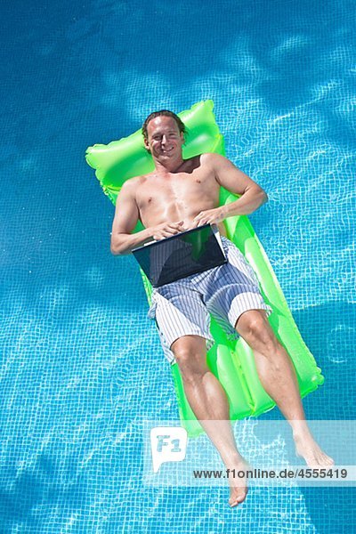 Man floating on inflatable raft and working on laptop
