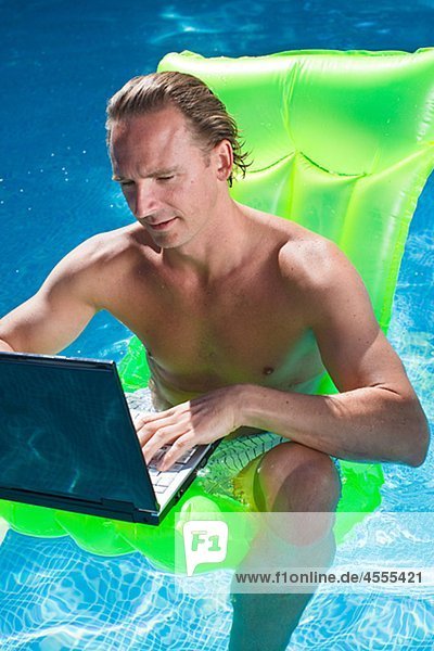 Man sitting on inflatable raft and working on laptop