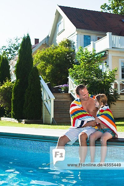 Father and daughter sitting at the edge of swimming pool