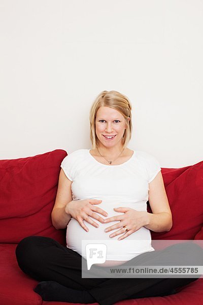 Porträt von schwangeren Frau berühren Magen auf sofa