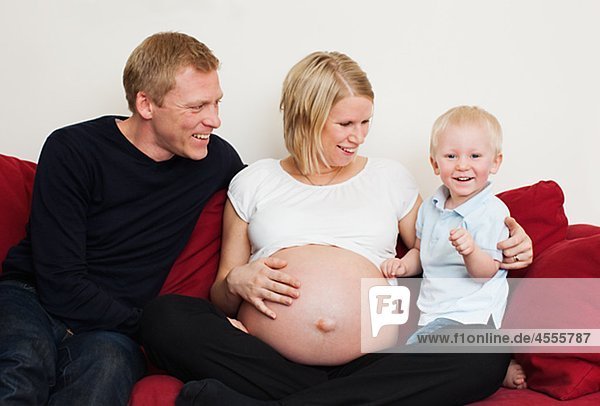 Schwangere Frau mit Partner und Sohn auf Sofa sitzen und lächelnd