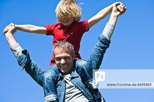 Piggyback Portrait von Vater und Sohn gegen Wolkenloser Himmel in hellem Sonnenlicht