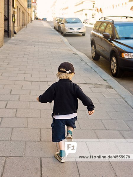 Rear view of boy running down sidewalk