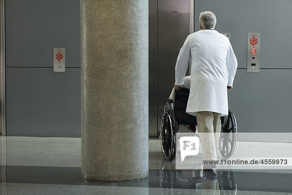 Arzt schiebt Patient im Rollstuhl in Richtung Aufzug
