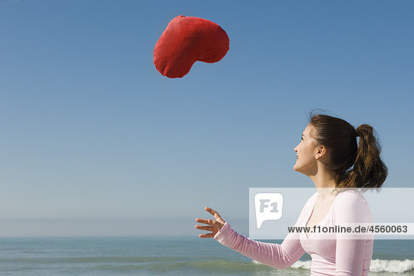 Preteen Mädchen am Strand werfen gestopftes herzförmiges Spielzeug in die Luft