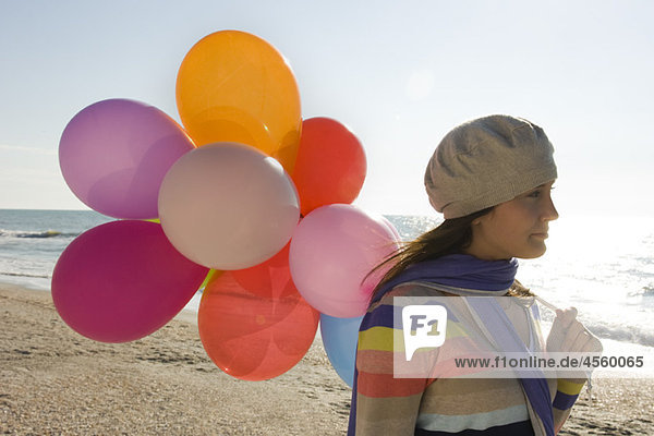 Preteen Mädchen mit einem Haufen Luftballons  die am Strand laufen.