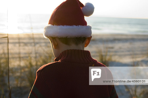 Junge auf Entdeckungsreise mit Nikolausmütze  Strand im Hintergrund