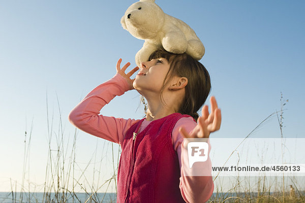 Junges Mädchen im Freien balanciert ausgestopften Eisbären auf dem Kopf