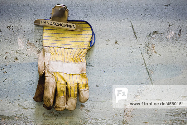 Arbeitsschutz-Handschuhe  die durch einen Binderclip an der Wand gehalten werden.