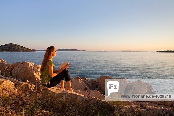 Kroatien  Zadar  Junge Frau mit Buch mit Blick auf den Strand