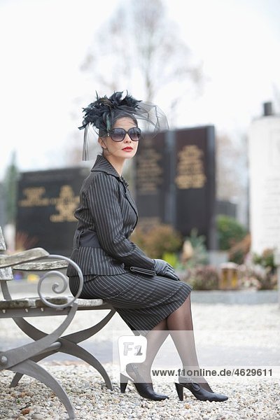 Junge Frau sitzt auf einer Bank auf dem Friedhof.