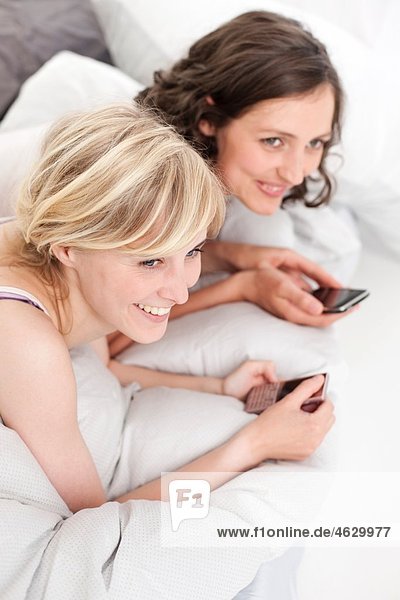 Young women on bed with mobile phone  smiling