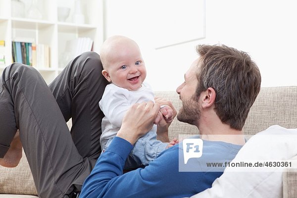 Father and baby boy (6-11 Months) having fun on sofa