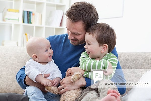 Deutschland  Bayern  München  Vater mit seinen Kindern auf dem Sofa  lächelnd