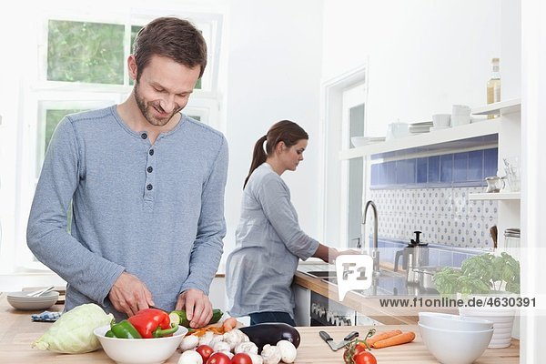 Mann hackt Zucchini in der Küche  Frau im Hintergrund