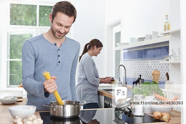 Mann kocht Spaghetti in der Küche  Frau im Hintergrund