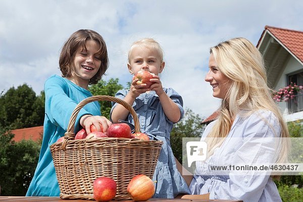 Deutschland  München  Mutter mit Kindern beim Essen von Äpfeln aus dem Korb