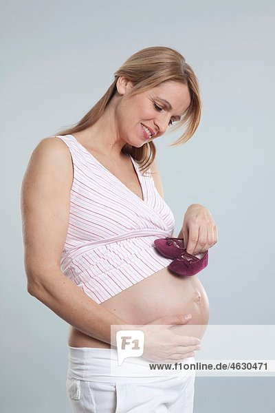 Schwangere mittlere erwachsene Frau mit Babyschuhen