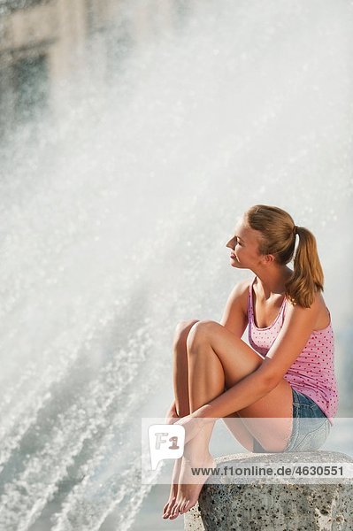 Young woman sitting at fountain