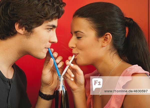 Germany  Munich  Young couple sharing a drink with straws in cafe