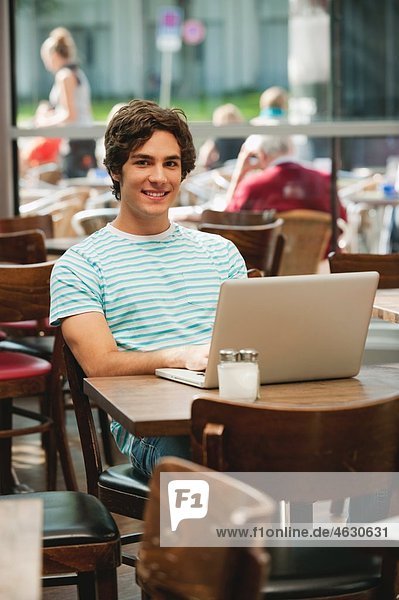 Young man with laptop in cafe  smiling  portrait