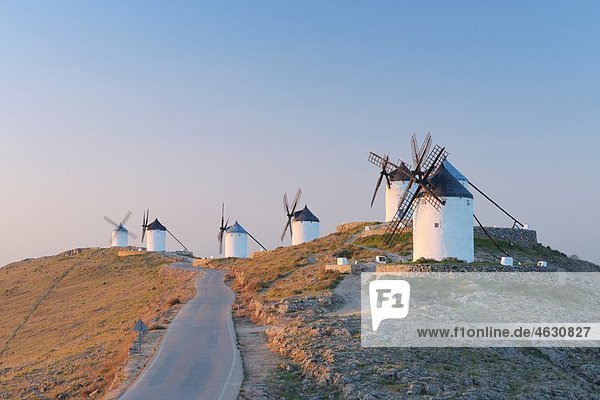 Spanien  Provinz Toledo  Kastilien-La Mancha  Reihe von Windmühlen mit Landstraße bei Sonnenaufgang