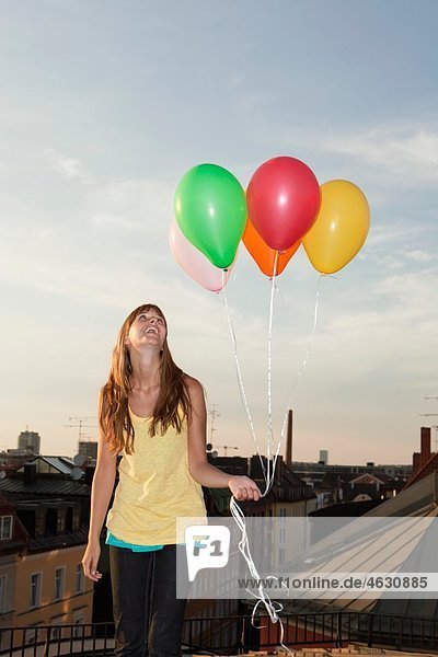 Junge Frau mit Ballons auf dem Dach  lächelnd