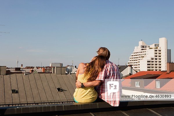 Deutschland  Bayern  München  Junges Paar auf dem Dach mit Stadt im Hintergrund
