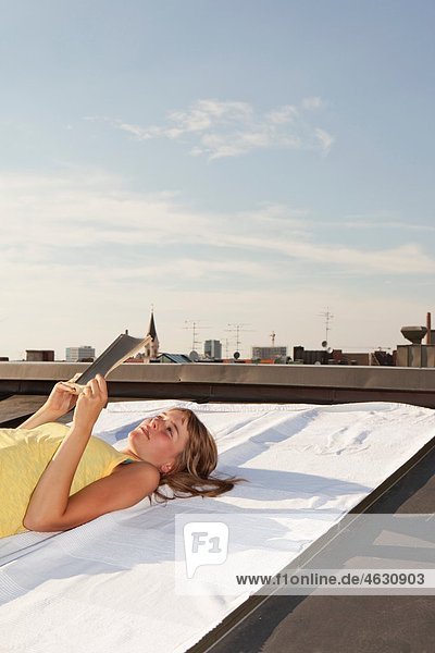 Junge Frau beim Lesen eines Buches auf einem Dach