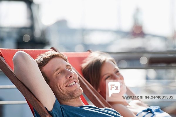 Germany  Hamburg  Couple relaxing in deck chair looking away  smiling