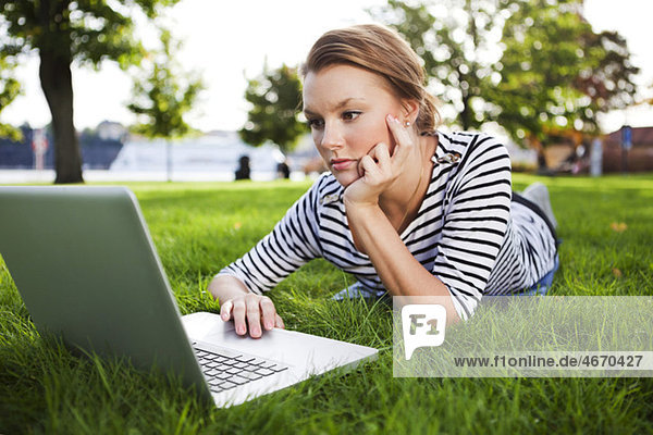 Frau im Gras liegend mit Computer