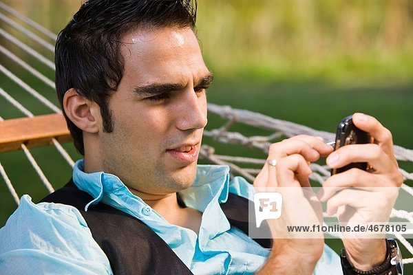 Young man with his cell phone in a hammock  Germany  Europe
