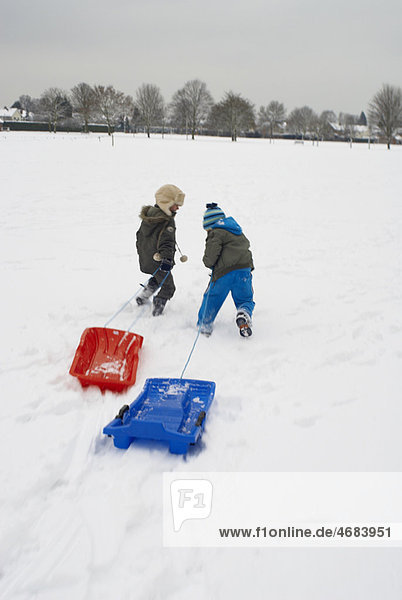 Boys running in snow with sledges