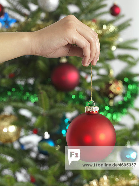 Hand holding Christmas bauble decorating a Christmas tree