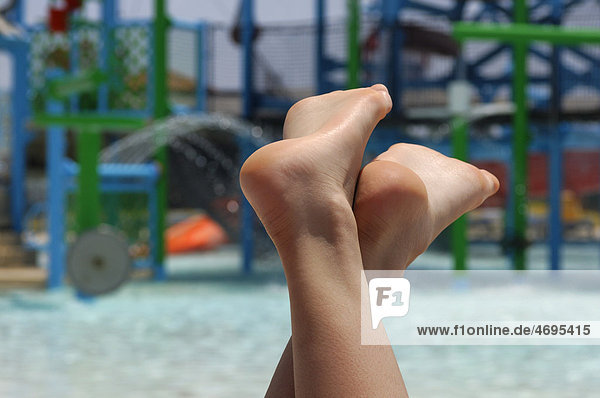 Nackte Füße einer jungen Frau die an einem Pool in einem Wasserpark entspannt