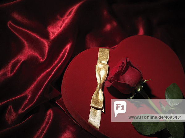 Rote herzförmige Geschenkschachtel mit goldener Schleife und roter Rose