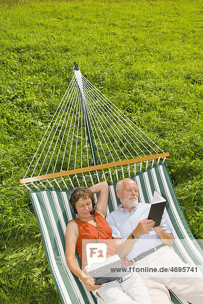 Senioren Paar in Hängematte  Frau mit Headset und Netbook  Laptop  Mann liest Buch