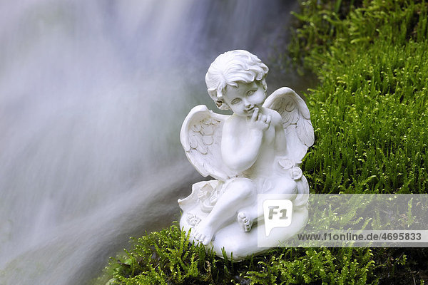 Porcelain angel figure on moss at a waterfall