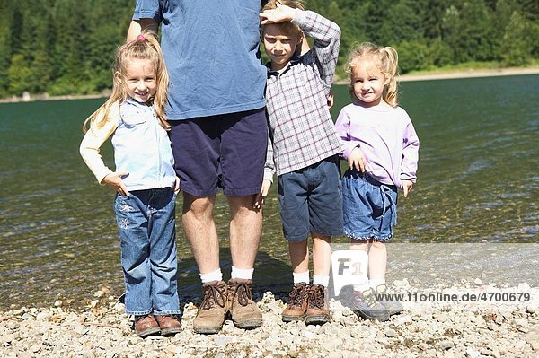 Three children standing with their father by a lake.